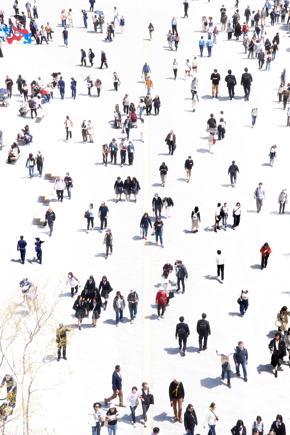 Diverse people in a sunlit public square with shadows.